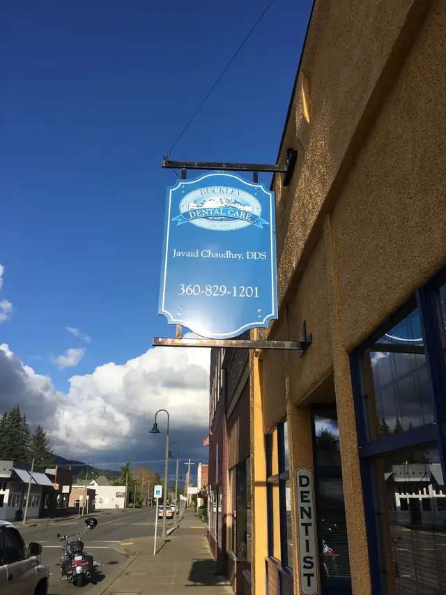 The blue Buckley Dental Care sign hanging over Main Street in downtown Buckley, with clouds over the foothills